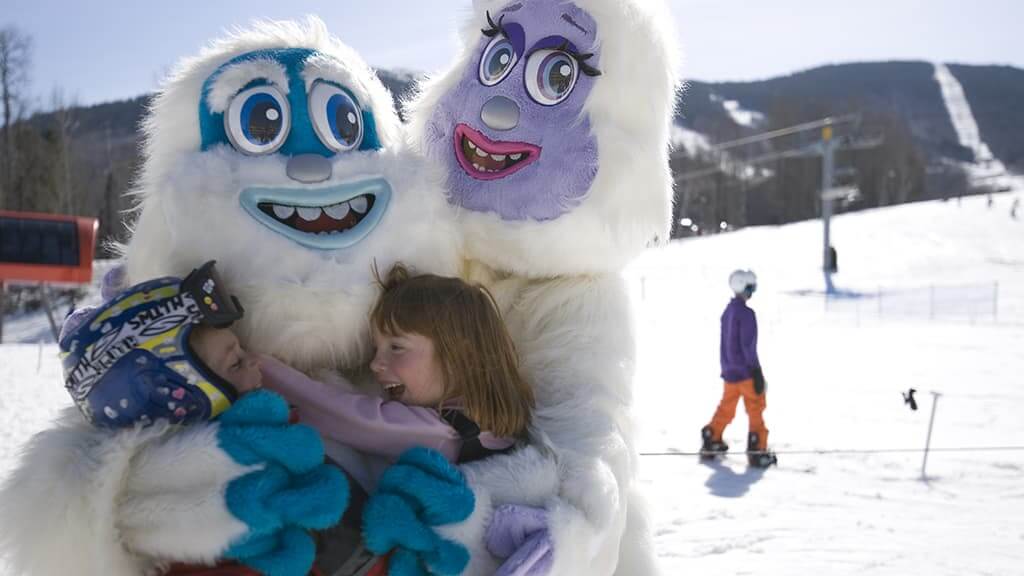 Sunday River mascots Eddy and Betty hugging a young girl during her family spring vacation