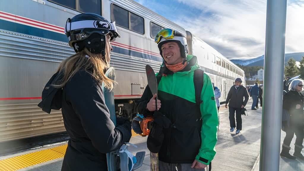 Man and woman standing with ski gear next to an Amtrak train at Winter Park Resort