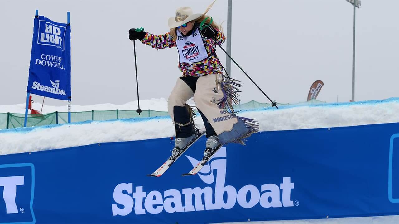 Woman dressed in western gear skiing over a jump during the Steamboat Cowboy Downhill