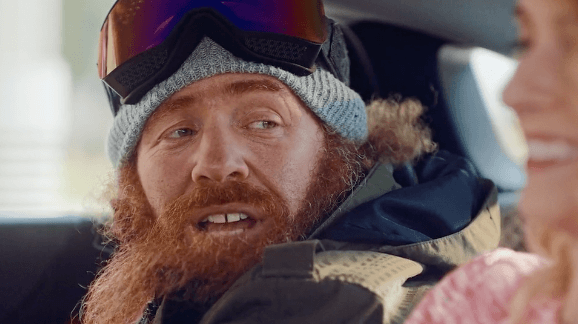 Man with big red beard, winter hat and goggles sitting in a car.