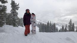 Adaptive athlete Brittani Coury standing with her snowboard at the top of a run on a cloudy day
