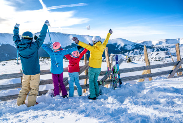 A family in ski gear standing at the top of a ski hill holding their arms in the air cheering