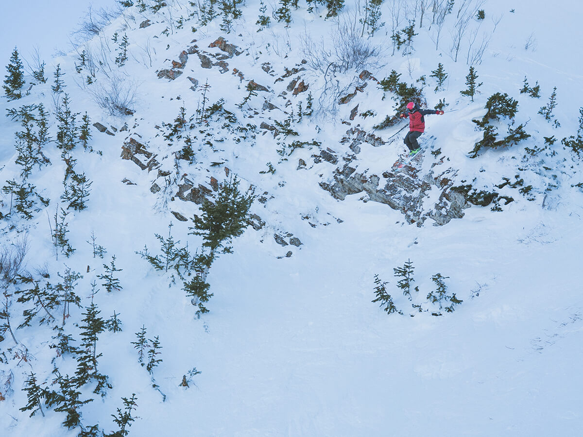 Skier jumping from a rocky cornice in fresh powder