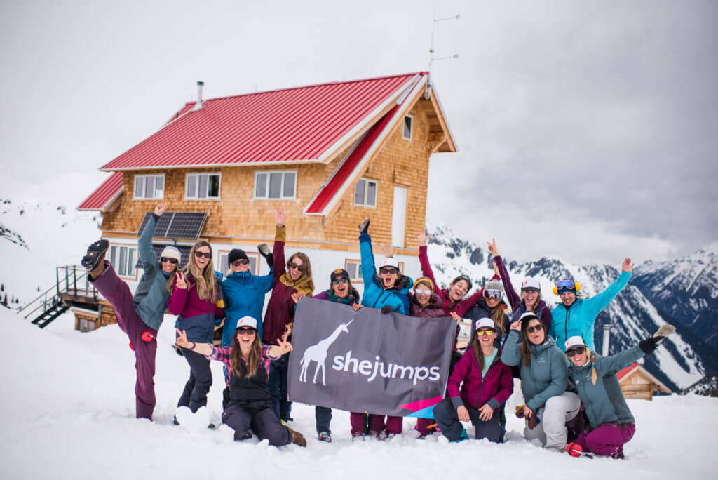 A group of women holding a SheJumps sign on the top of a mountain.