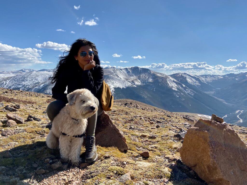 Alenka Balderrama, a BIPOC woman with her dog at the top of a mountain. One of the Ikon Pass Scholarship winners.