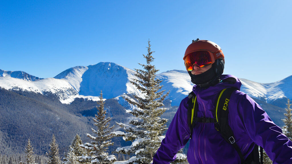 Man in ski gear standing outside with a snowy mountain range behind him