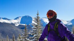 Man in ski gear standing outside with a snowy mountain range behind him