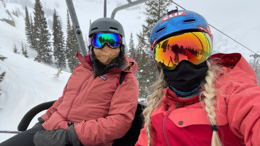 Two women in ski gear and face masks riding a chairlift