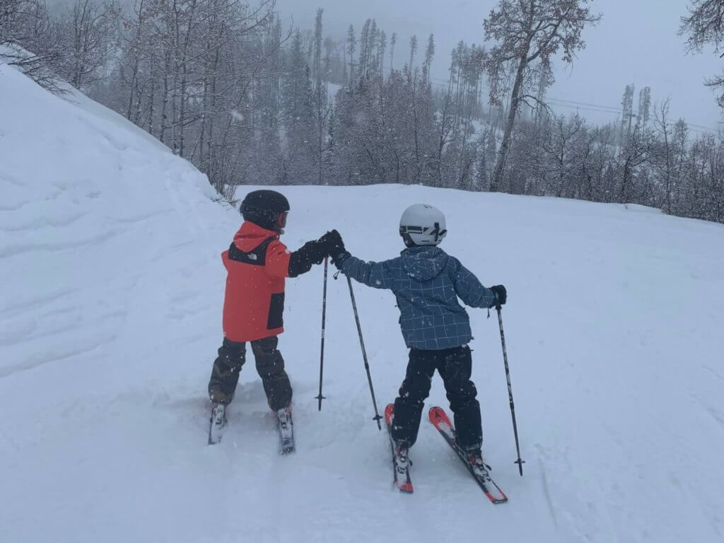 Two young boys in ski gear giving each other a high five on a snowy day on the mountain