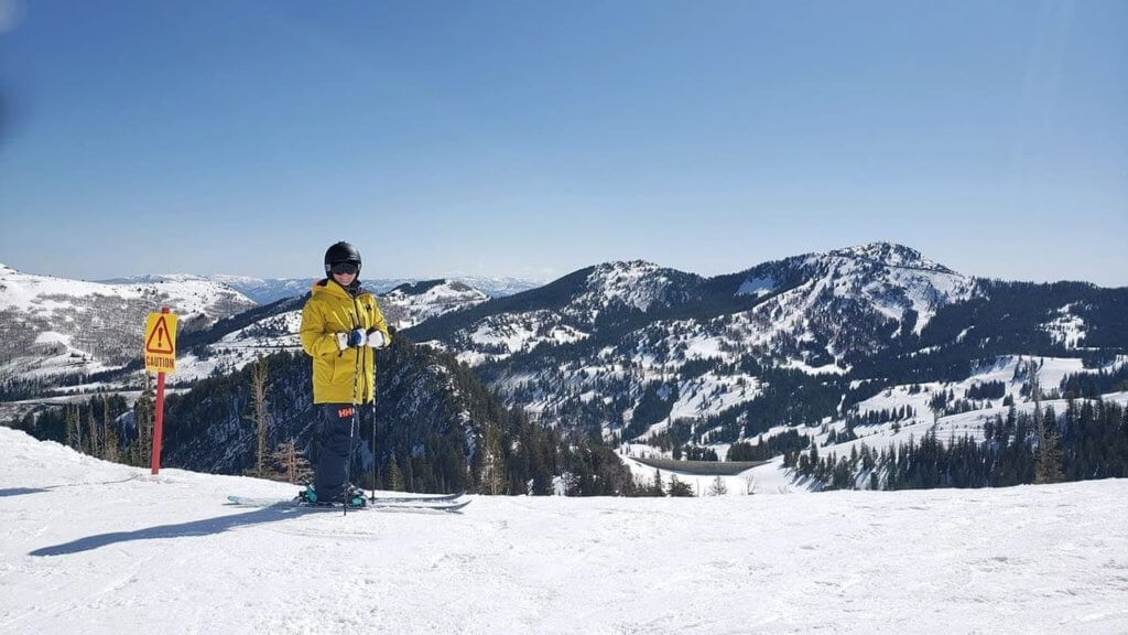 Female skier in ski gear standing at the top of a ski run with a mountain view in the background