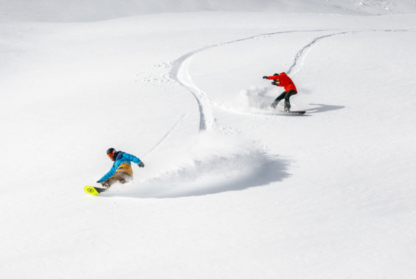 Two snowboarders riding through deep powder
