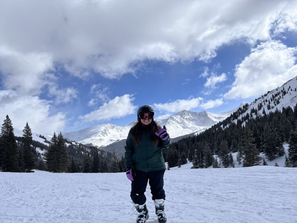 SheJumps scholarship recipient Jessica Beltran standing at the base of a snowy Copper Mountain in Colorado.