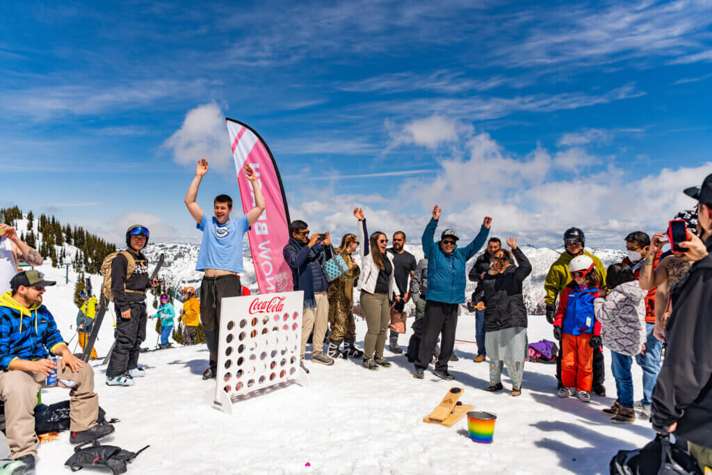 Group of people playing an oversized game of connect four at the top of a snowy ski hill.
