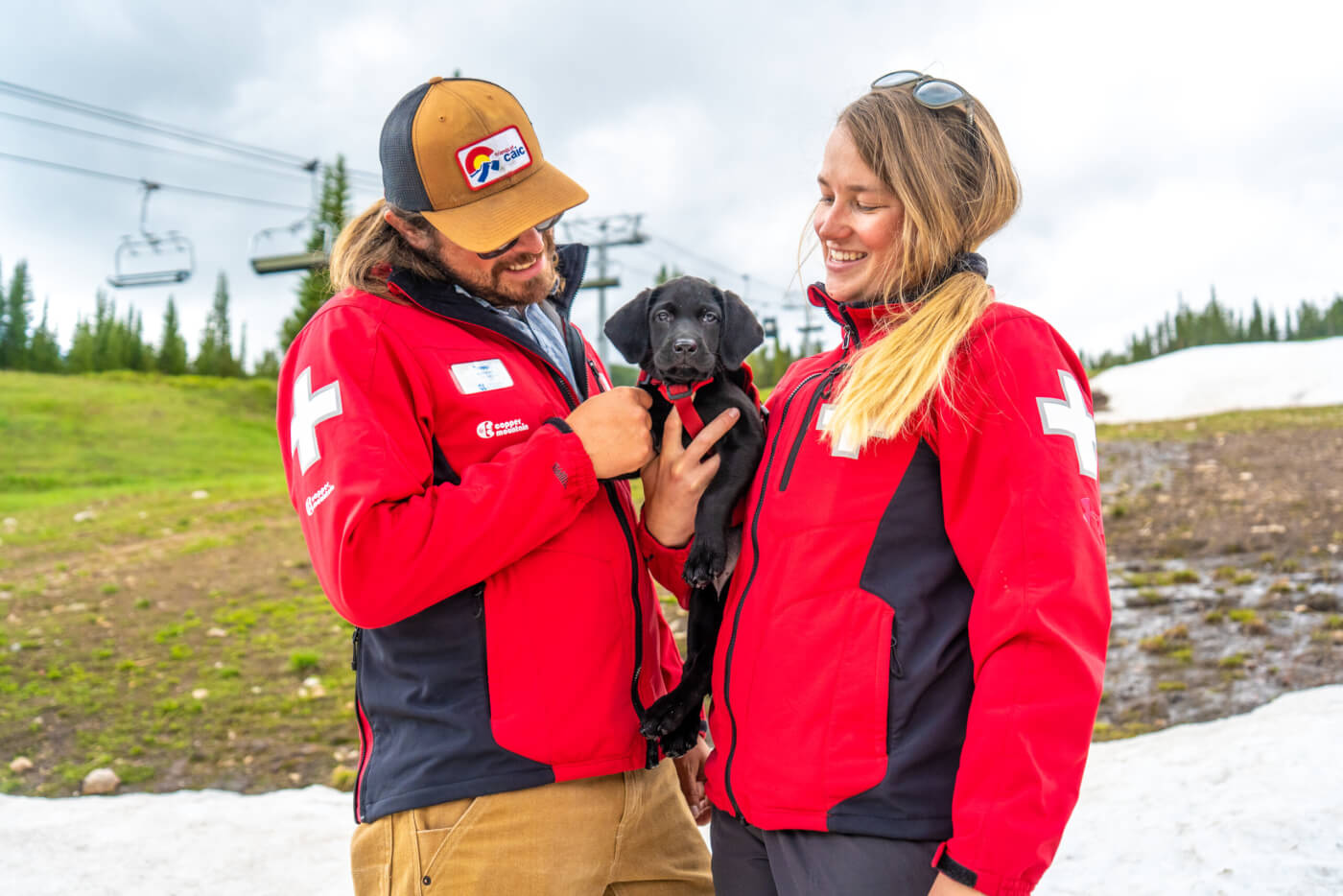 Two ski patrollers holding a puppy.