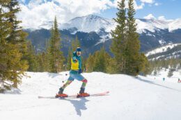 Skier dressed in retro gear points to camera as they descend down the mountain.