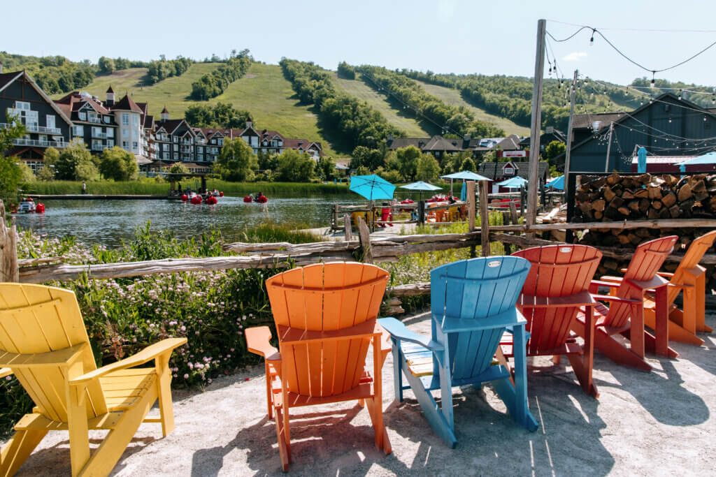 Group of colorful chairs facing a lake at the base of a mountain.