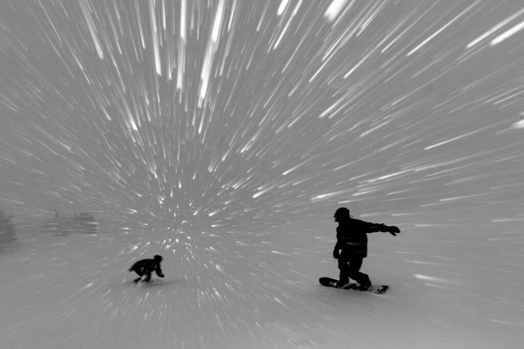 Black and white image of snowboarders silhouettes as they ride during a snowfall.