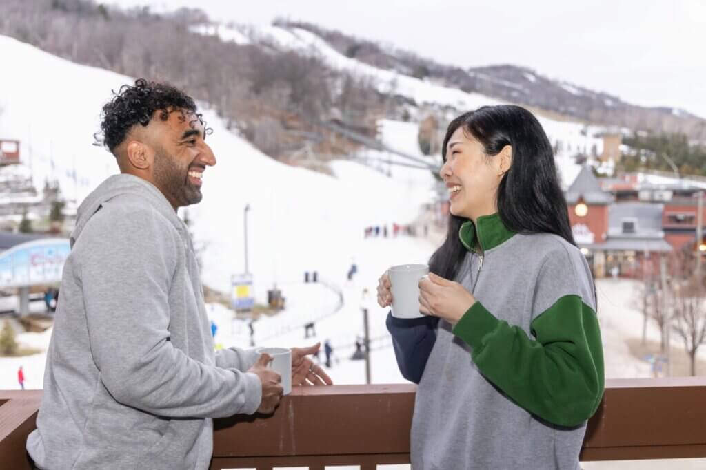 Two people enjoying coffee on their balcony overlooking a ski resort.
