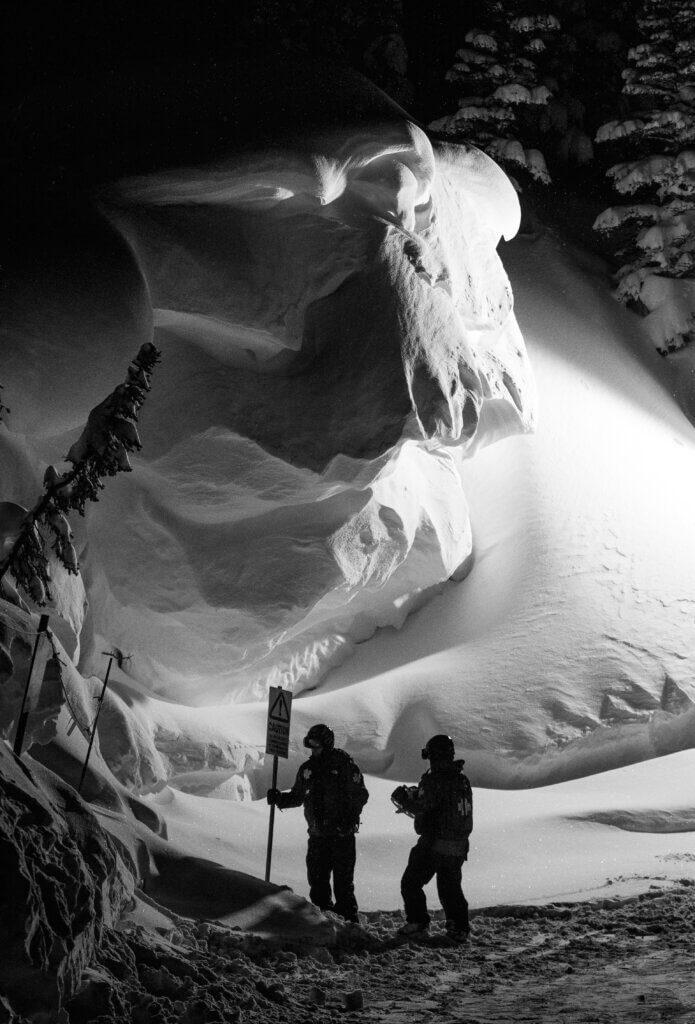 Black and white image of Ski Patrol silhouetted as they work at night.