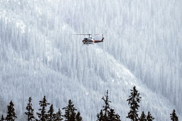 Helicopter flying in front of snow covered trees.