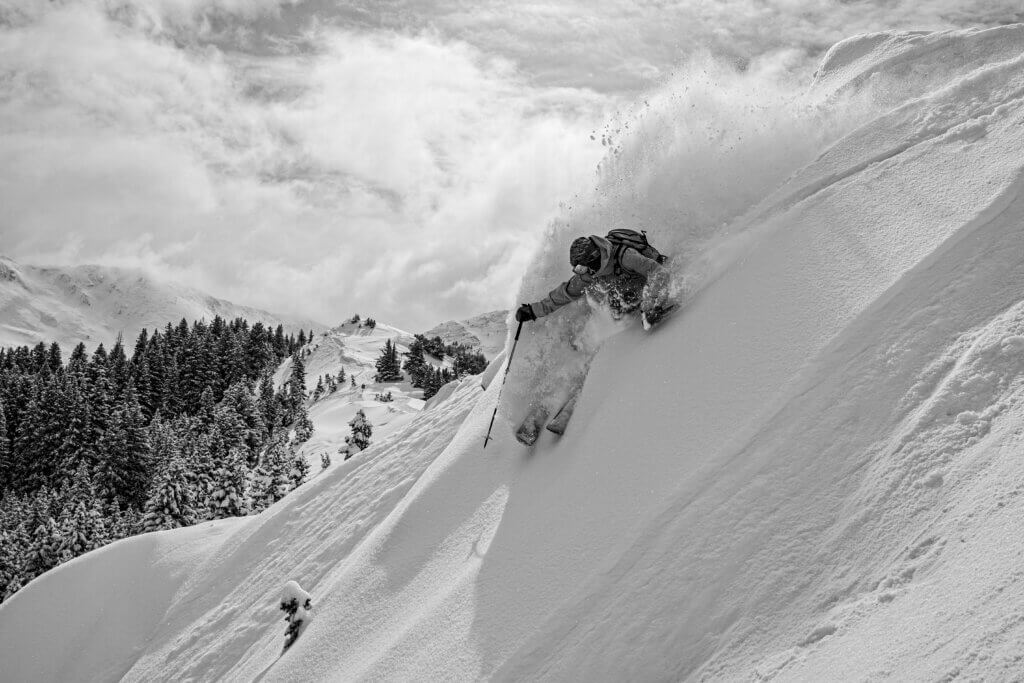 Black and white image of a skier carving through powdery snow.
