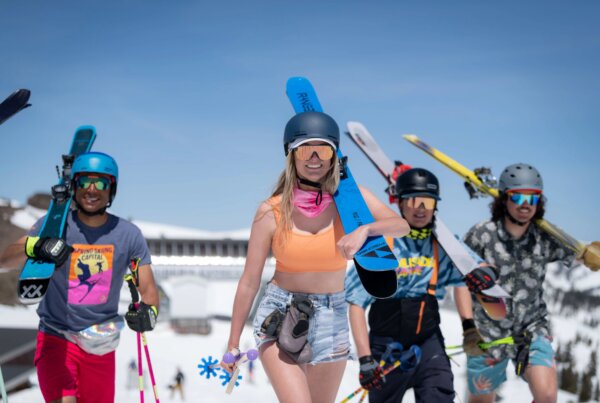 Group of spring skiiers headed to the mountain while dressed in warm weather gear.