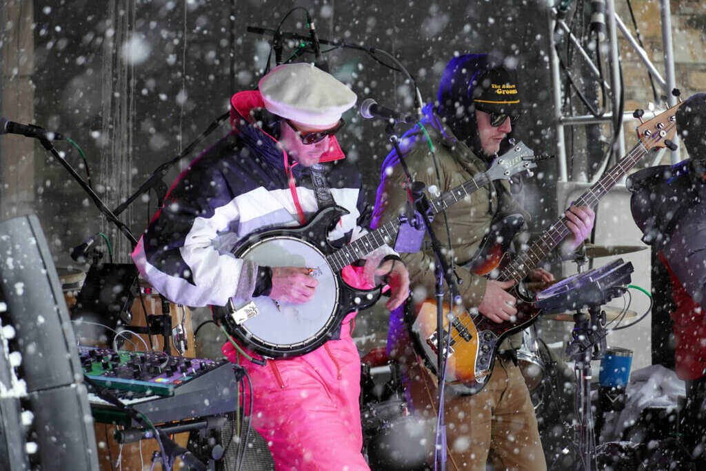 Two musicians playing during a music festival while snow falls around them.