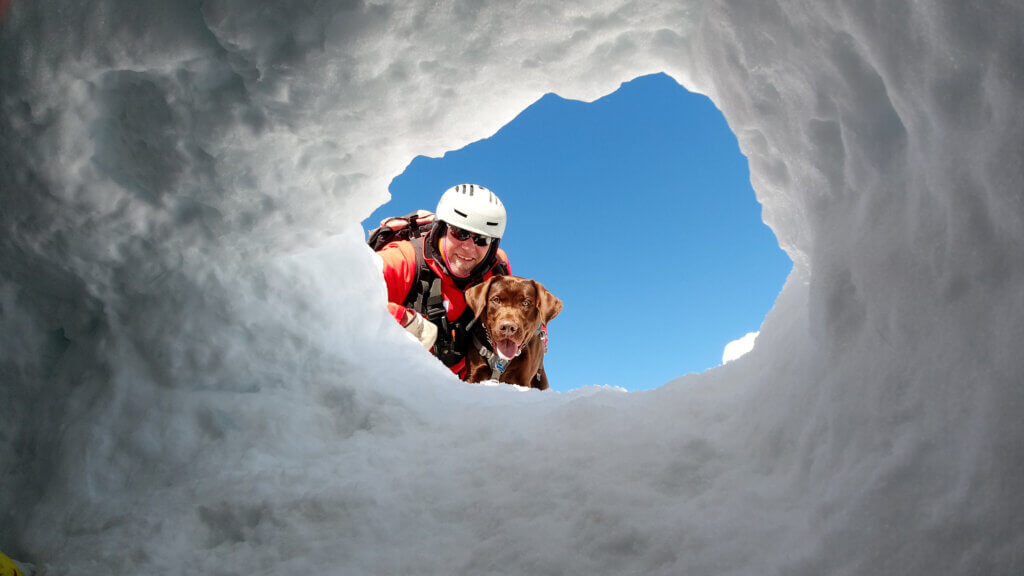 Patrol dog and handler looking down through a snow tunnel.