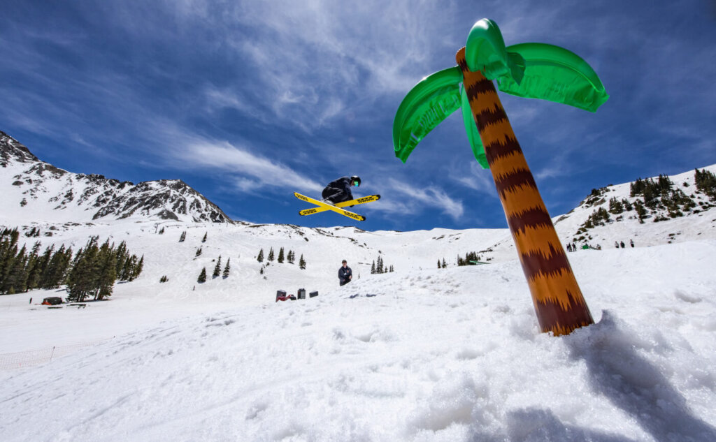 Inflatable palm tree sits in the snow while a skiier participates in spring skiing.
