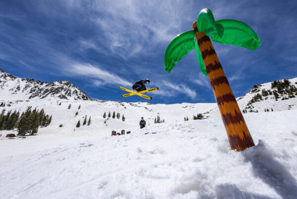 Inflatable palm tree sits in the snow while a skiier participates in spring skiing.