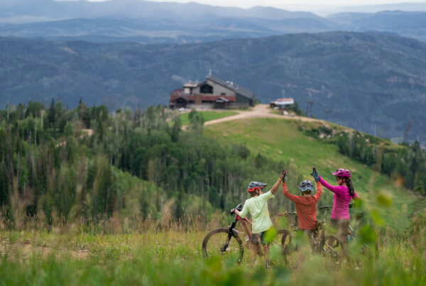 Three bike riders high-fiving while looking out at the view from a bike trail.
