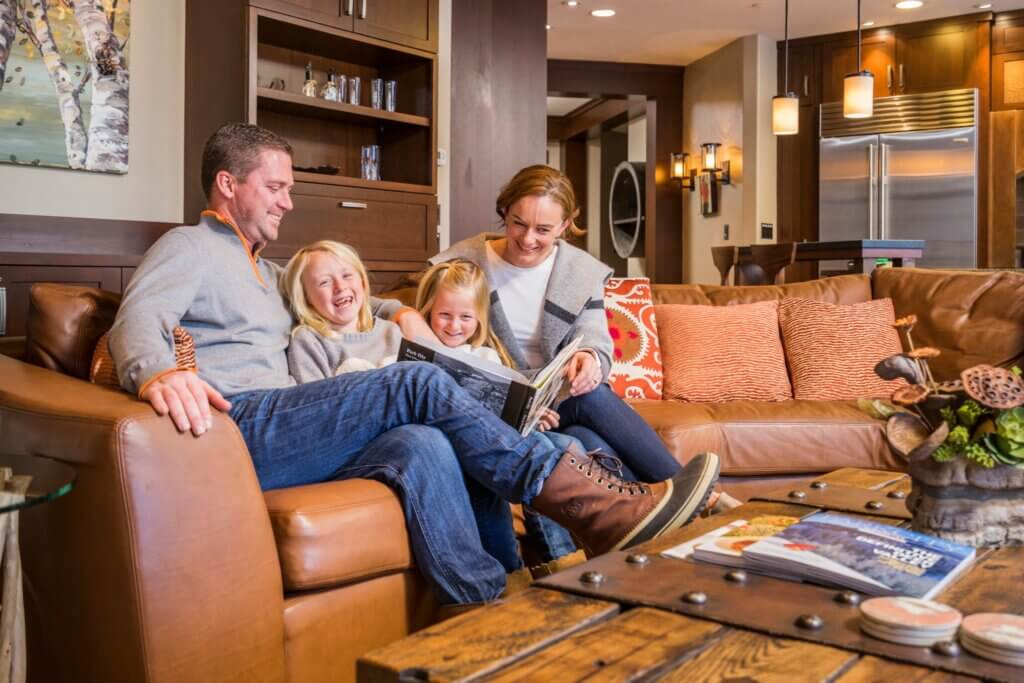 Family reading a book together while relaxing on the couch in their accommodations.