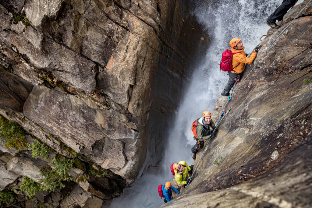 Group of people on a via ferrata route, climbing near a waterfall.