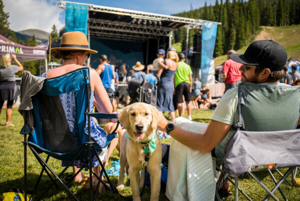 Two people sitting with a dog while at an outdoor summer festival.