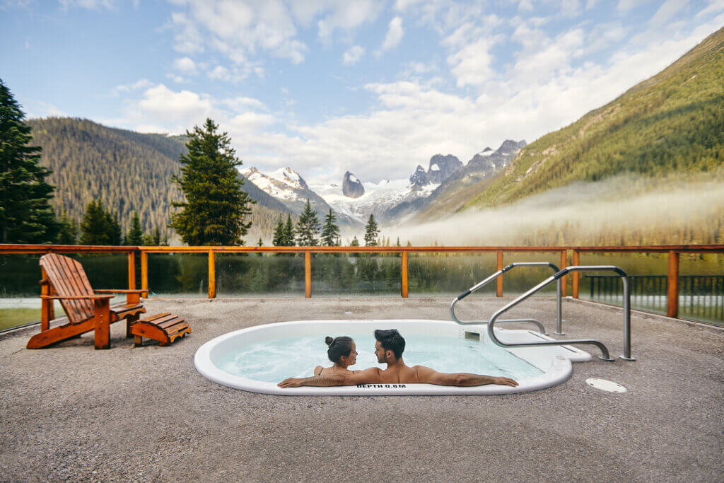 Two people relaxing in a roof top hot tub overlooking the mountains.