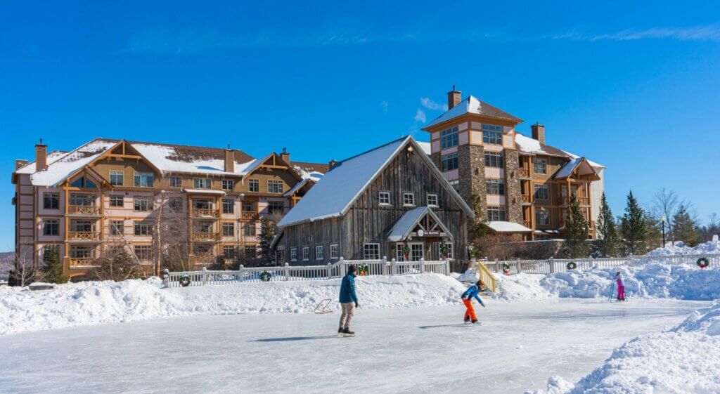 Group of people ice skating in front of a ski lodge.