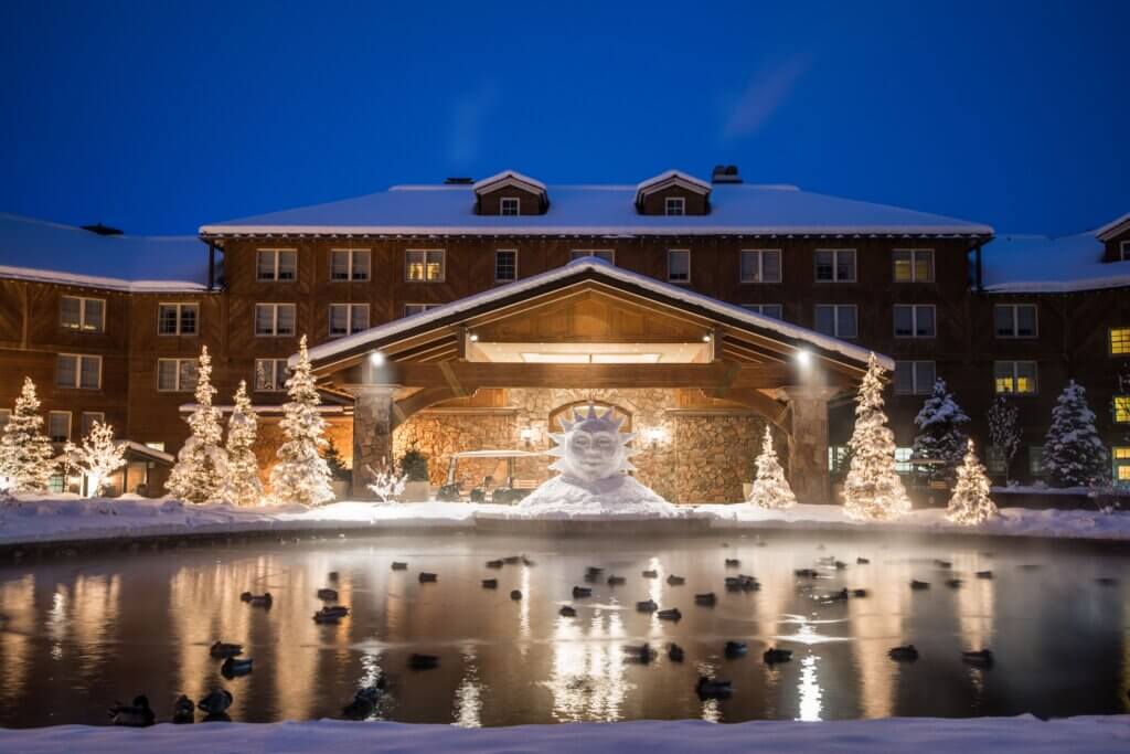 The exterior of a snowy and lit up Sun Valley Lodge at night.