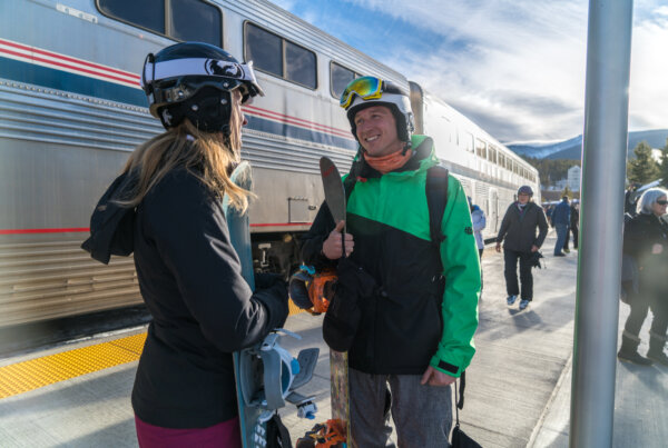 Two people with ski gear waiting outside of a train.