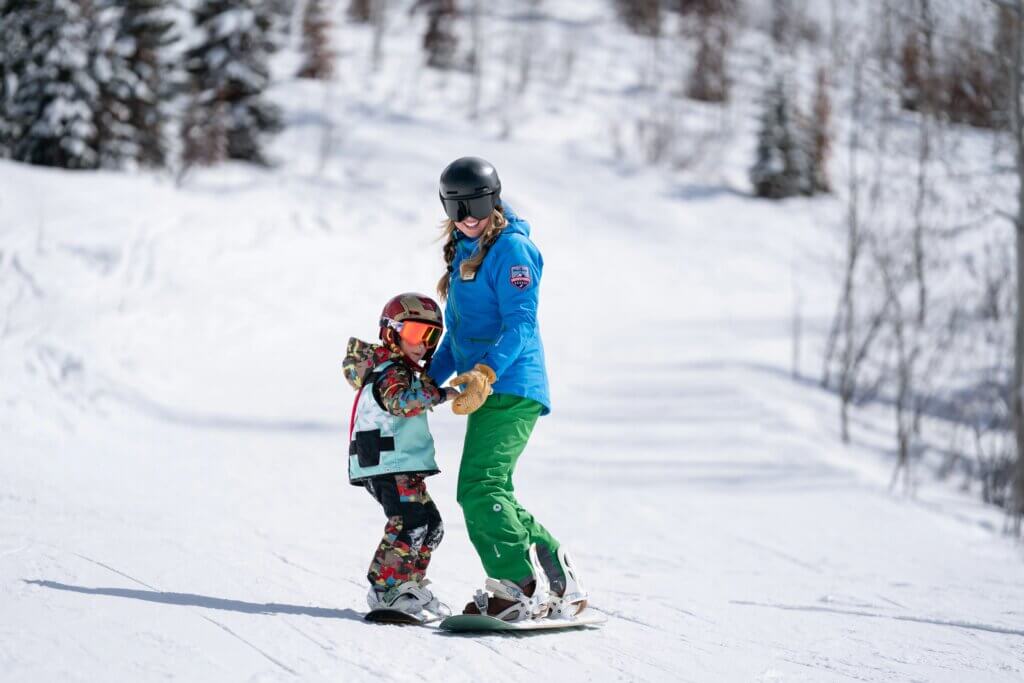 Snowboard instructor helping a child during a lesson.