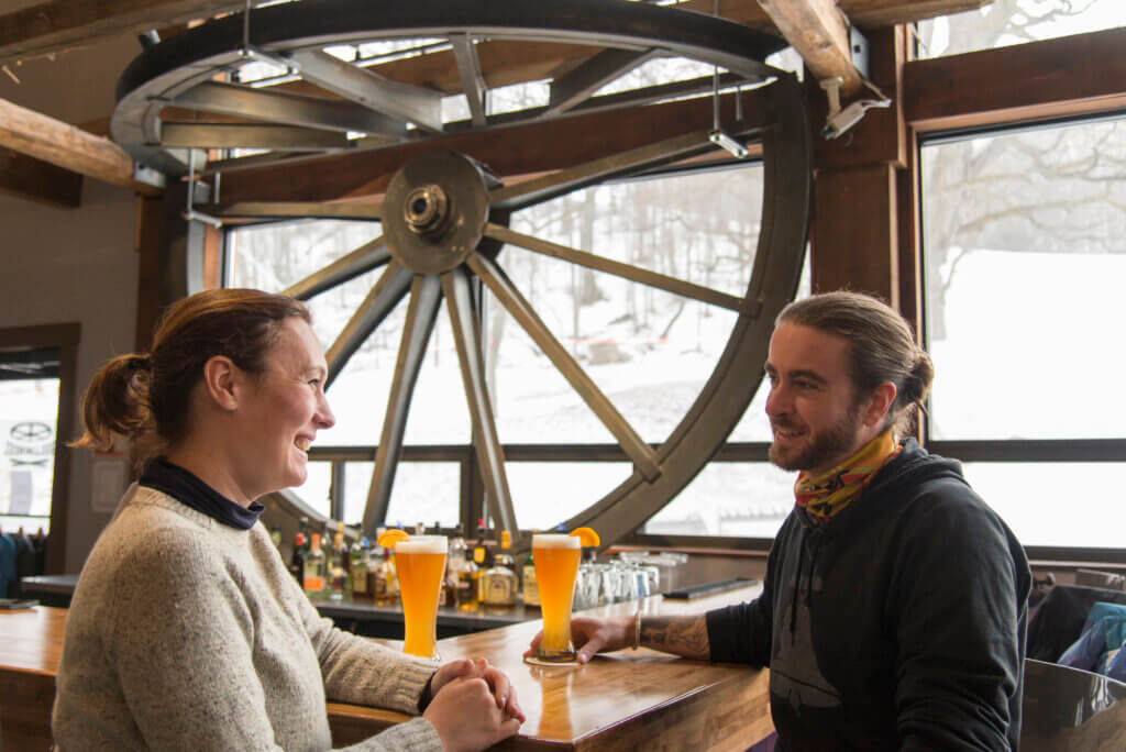 Two people sitting at a bar with beers.