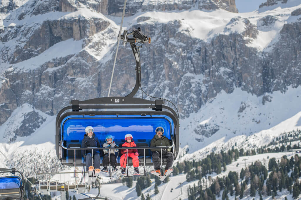 Group of people riding a chairlift with the mountains behind them.