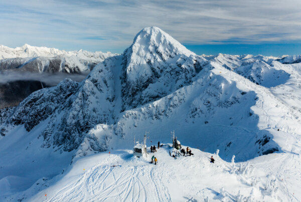 Snow covered mountain peak with a group of skiers and snowboarders waiting to descend the mountain.