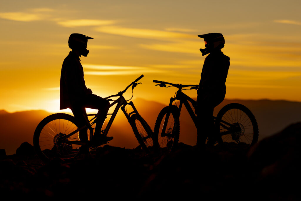 Two people sitting on mountain bikes at sunset