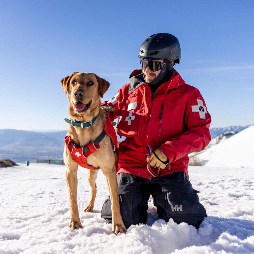 Avalanche rescue dog standing next to ski patrol team member.