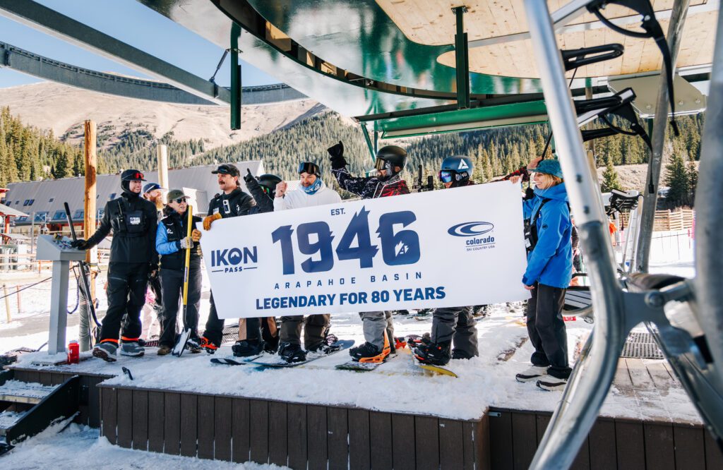 Group standing on stage with a banner to celebrate Arapahoe Basin's opening day 2026-2027 season
