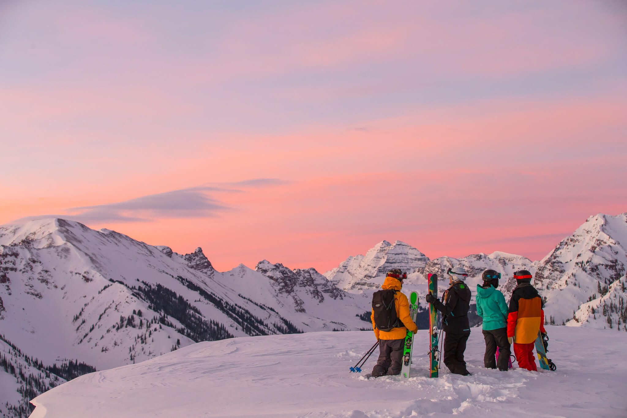 A group of four skiers and snowboarders looking out at the Maroon Bells at sunset