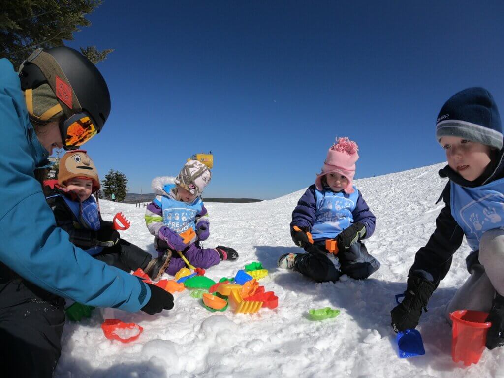 Toddlers playing with toys in the snow as part of Snowshoe's on-mountain daycare