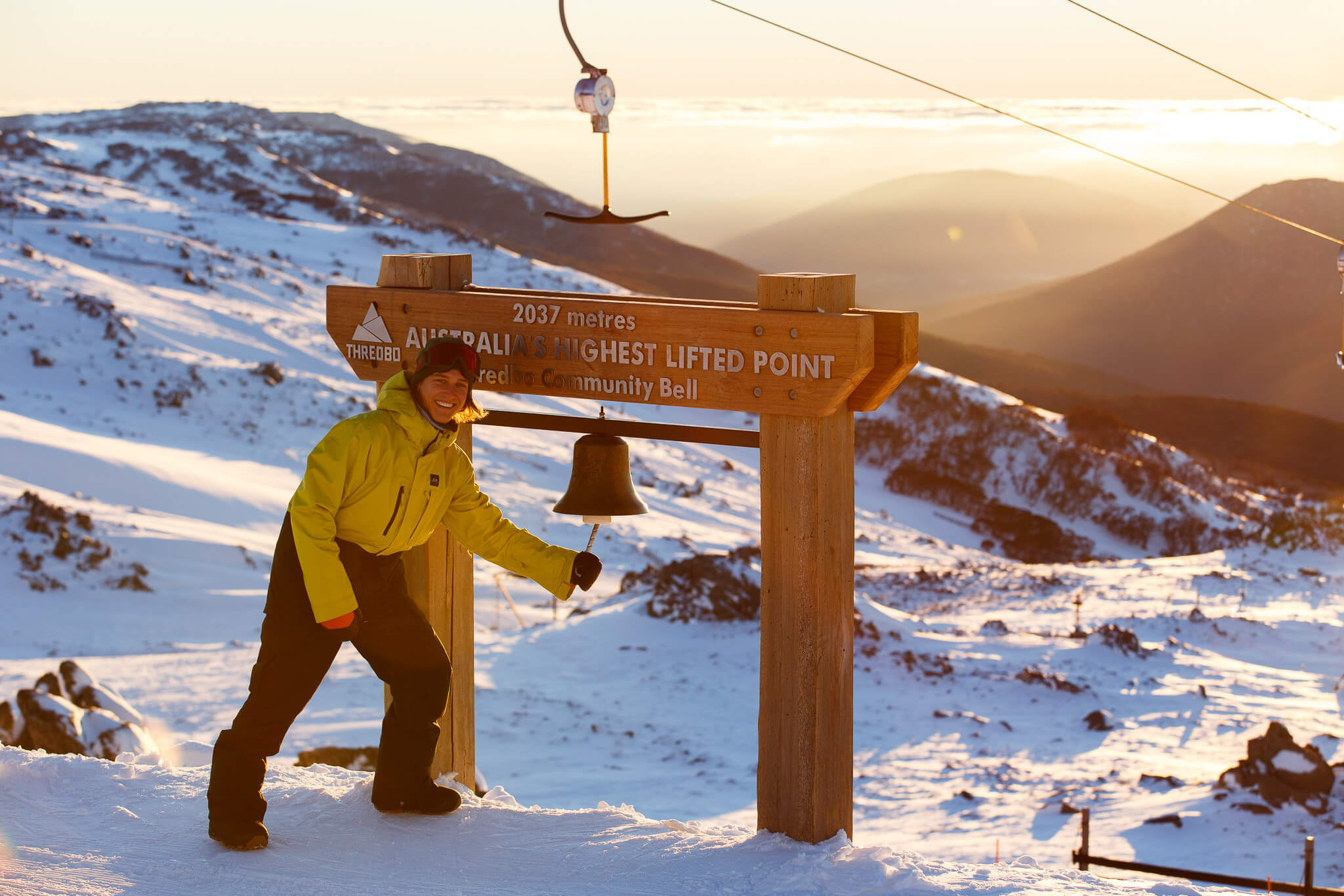 Man standing at the top of Thredbo at sunrise about to ring a bell