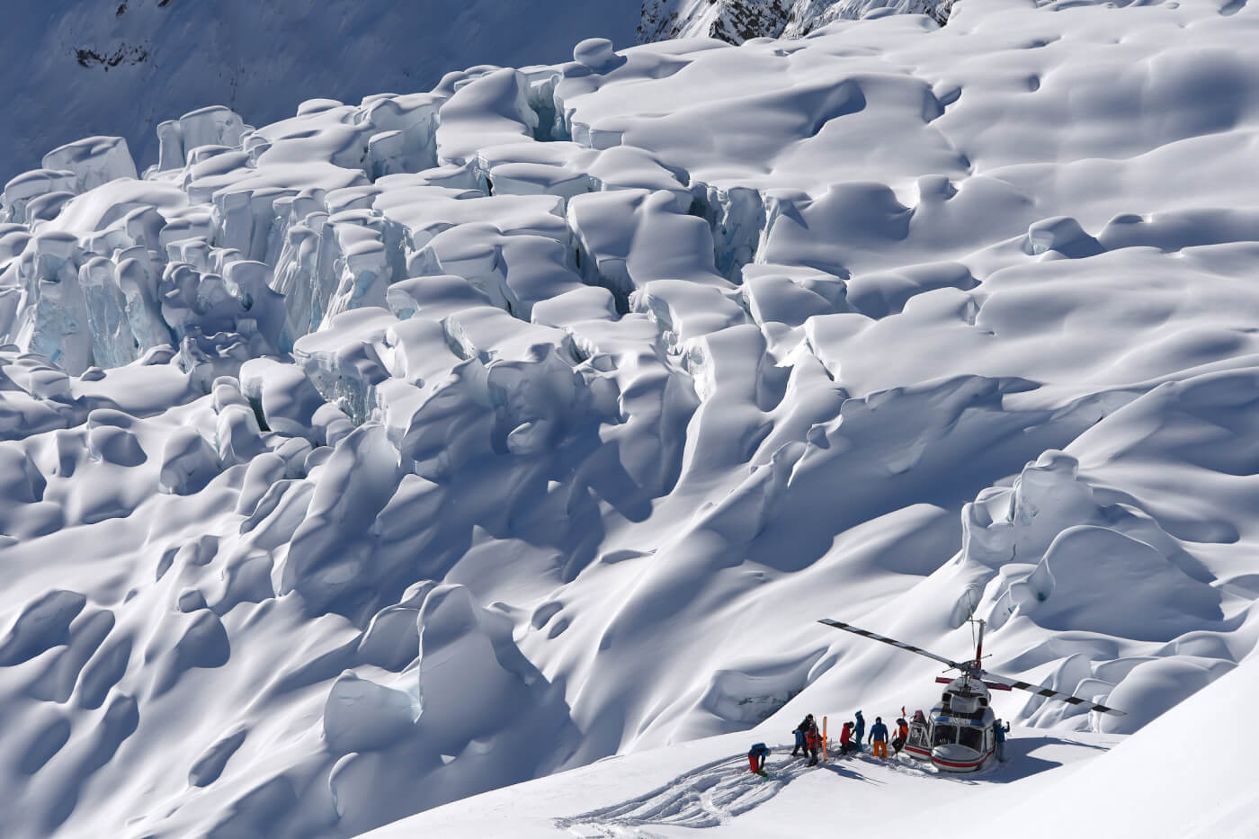 A helicopter sits on a snowy landscape with a group of people standing next to it