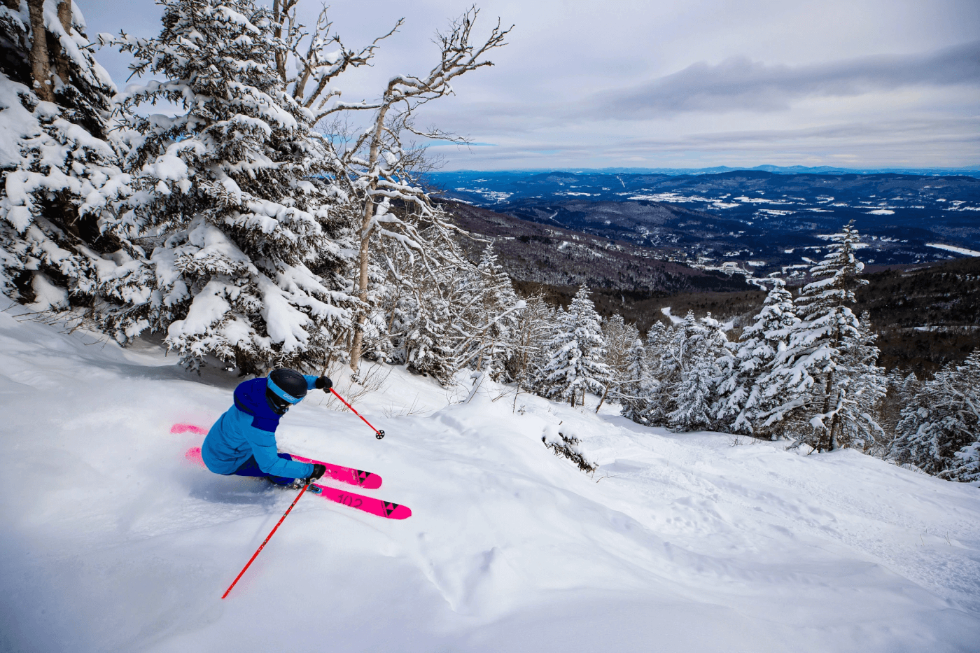 Skier going down a steep powdery run with a scenic mountain view in the background.